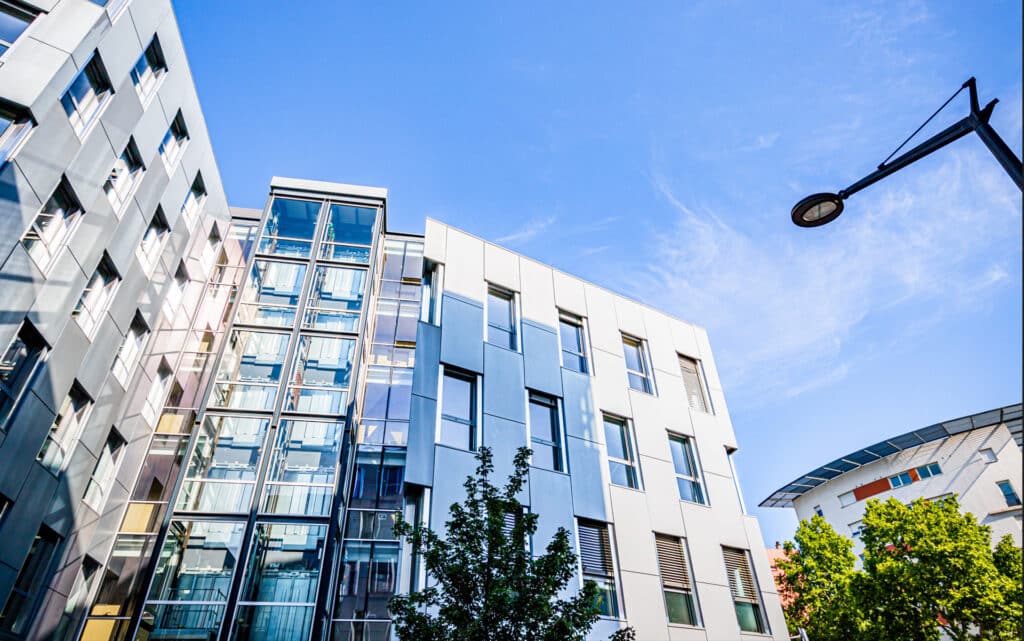 Immeubles à l'architecture moderne avec façade en verre et métal sous un ciel bleu dégagé.