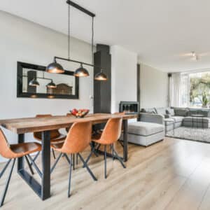 Salle à manger style industriel avec table en bois et chaises cuir ouvrant sur un salon moderne lumineux.