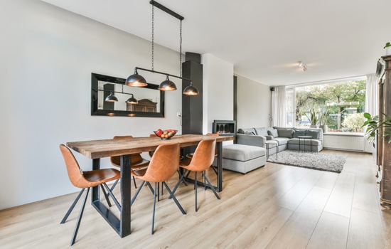 Salle à manger style industriel avec table en bois et chaises cuir ouvrant sur un salon moderne lumineux.